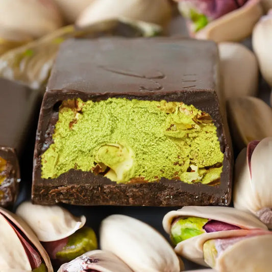 Close-up of a chocolate bar with green pistachio filling surrounded by pistachios.